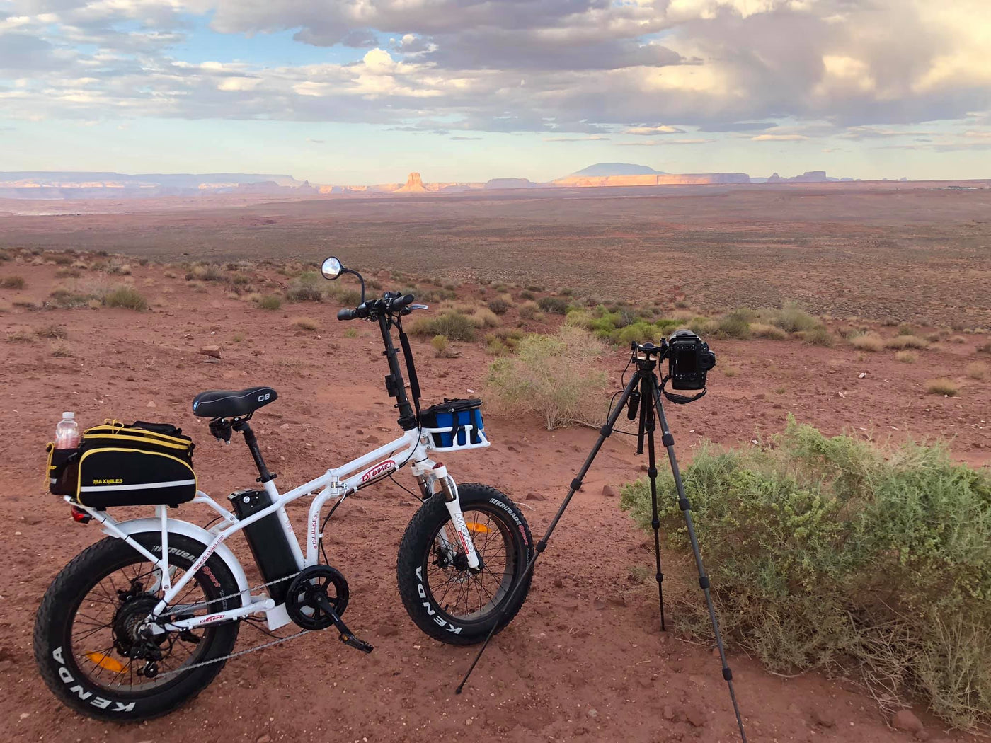 A DJ Folding Bike fat tire e-bike equipped with trunk and front bags next to a camera in the Arizona desert