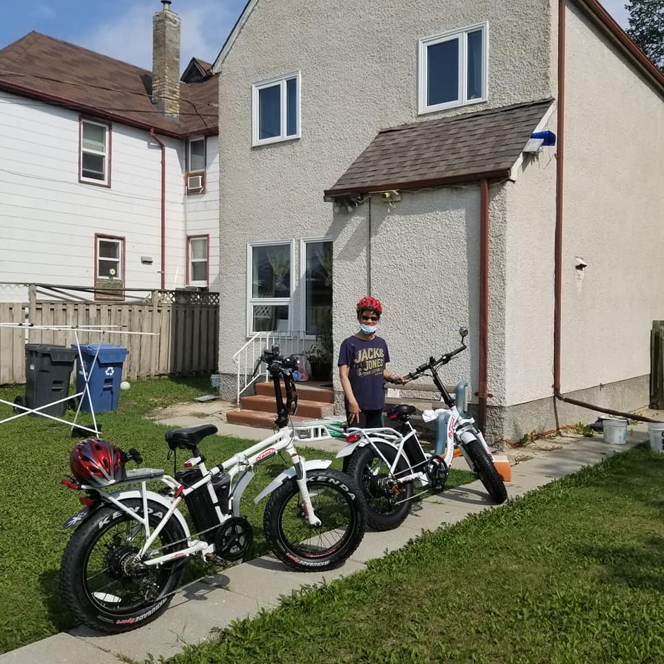 A woman poses with a DJ Folding Bike fat tire e-bike and a DJ Folding Bike Step Thru step-through fat tire e-bike on a path in front of a house