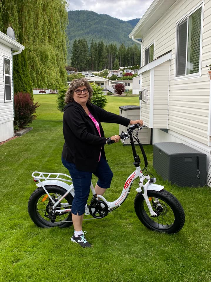 A smiling customer riding a DJ Folding Step Thru fat tire e-bike on grass in front of a house